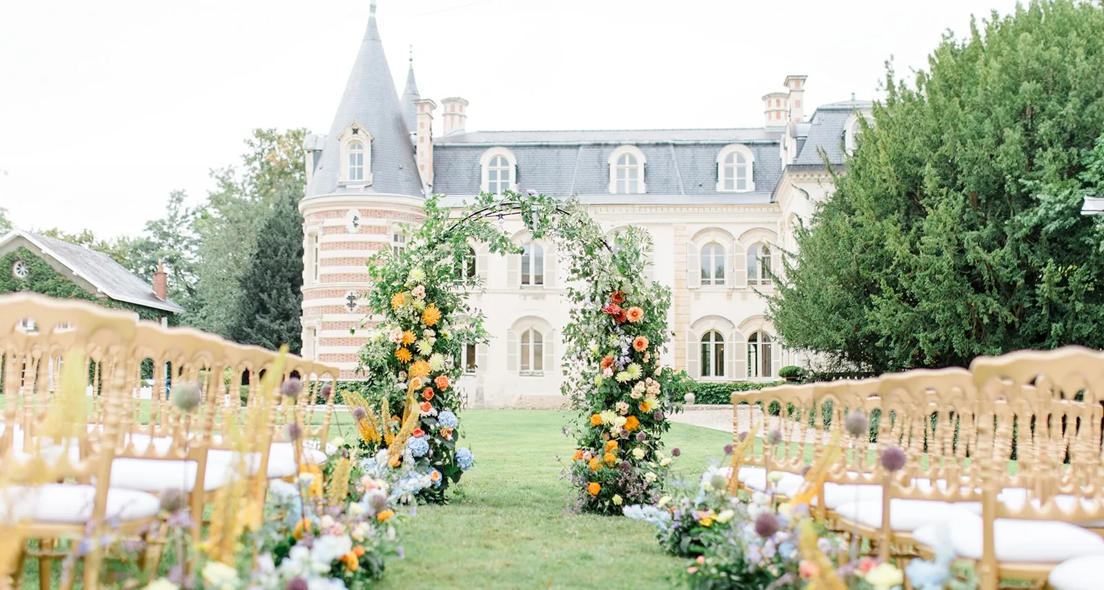 A flower arch and gold chairs on the lawn in front of the château